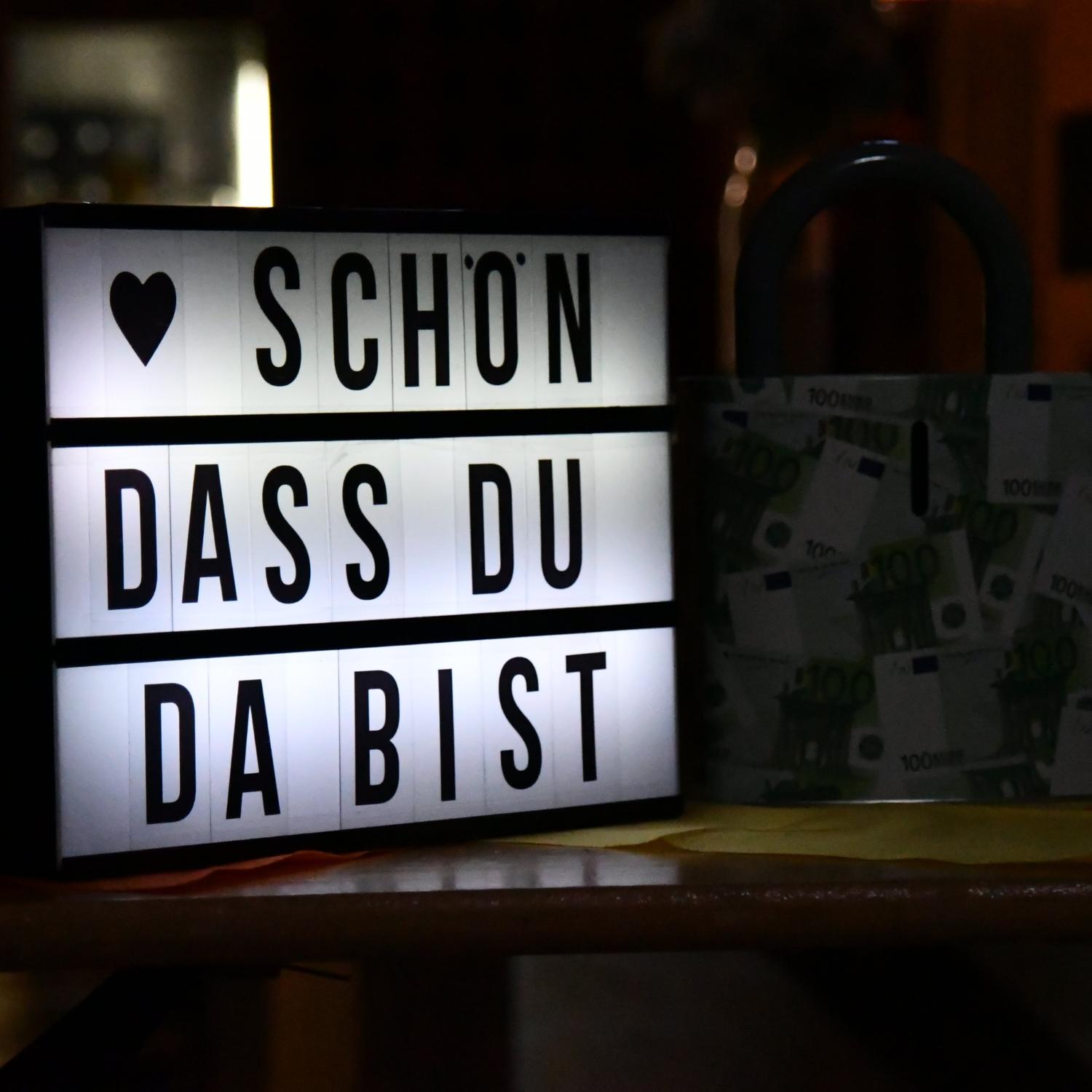 Leuchtbox mit dem Text „Schön, dass du da bist“ neben einer Geschenkbox.